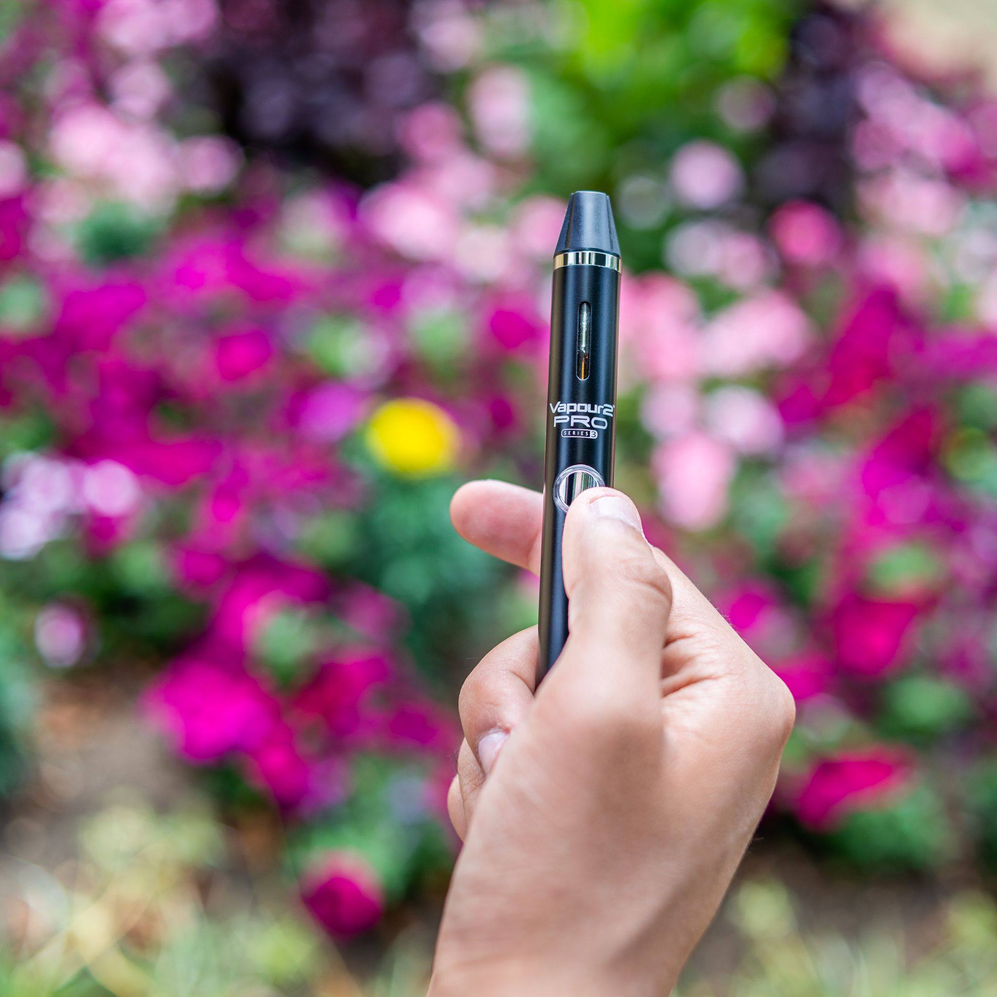 hand of man holding vape in front of flowers